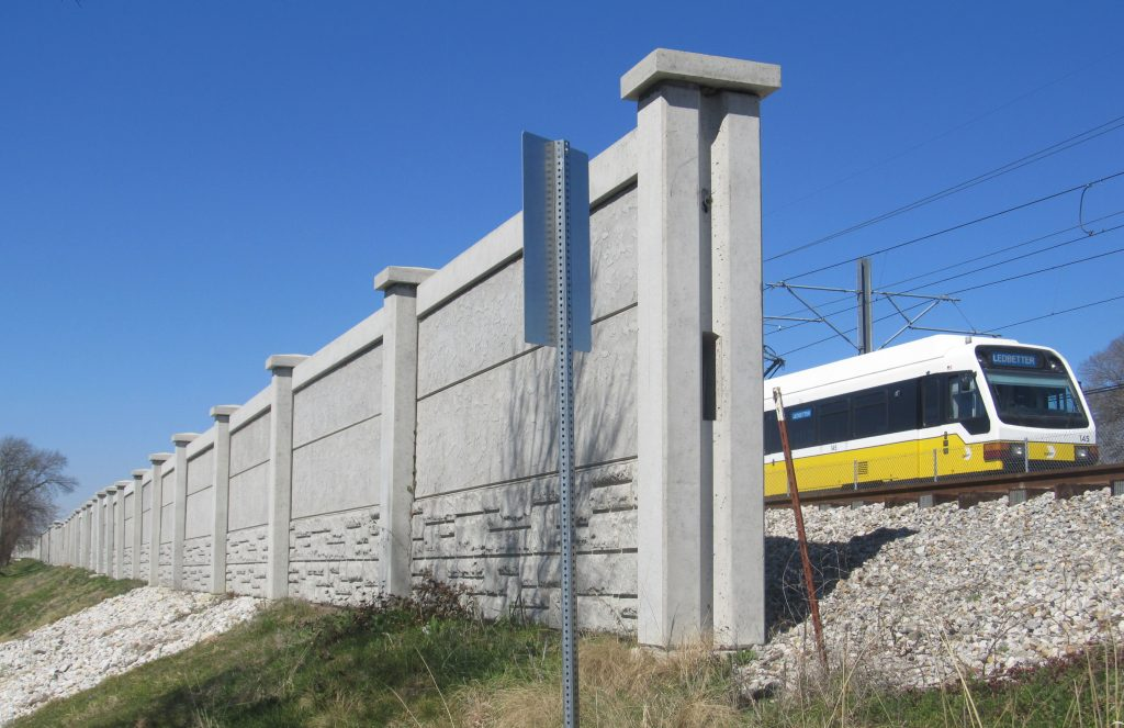 Wall blocking view of train with overhead catenary wires